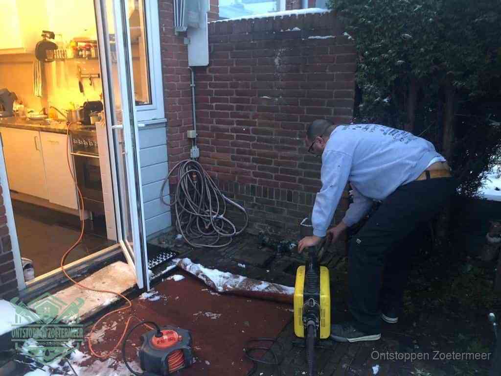 Een monteur werkt buiten bij een open riool-/grondput met een elektrische ontstoppingsmachine om een verborgen afvoerprobleem op te sporen in Zoetermeer