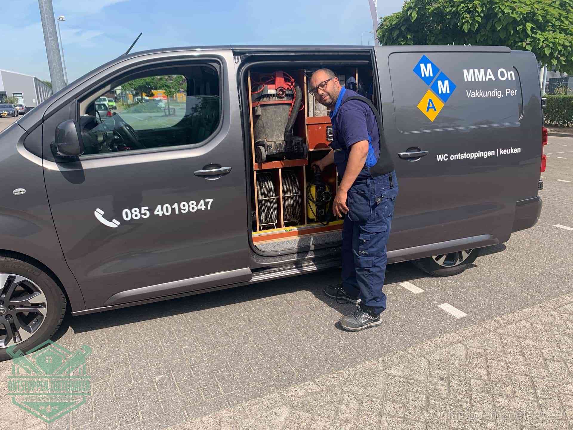 Een monteur bij de open schuifdeur van zijn bedrijfsbus op een parkeerplaats, klaar om de oorzaak van terugkerende afvoerverstoppingen aan te pakken in Zoetermeer