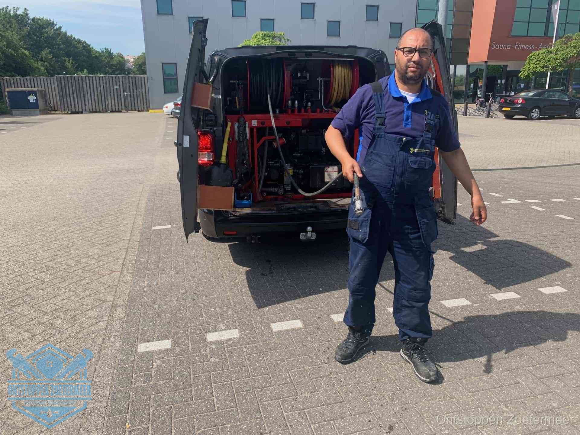 Een monteur bij zijn bestelbus met een hogedruk- en rioolreinigingsunit, klaar om de oorzaak van terugkerende wc-verstoppingen aan te pakken in Zoetermeer