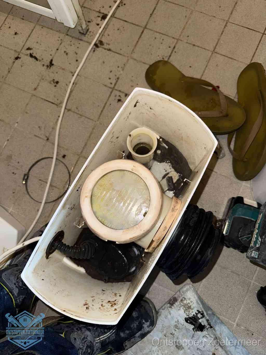 Een gedemonteerde toiletpot op de vloer met ontstoppingsveer en gereedschap ernaast, het verwijderen van een vastzittend voorwerp uit de wc in Zoetermeer