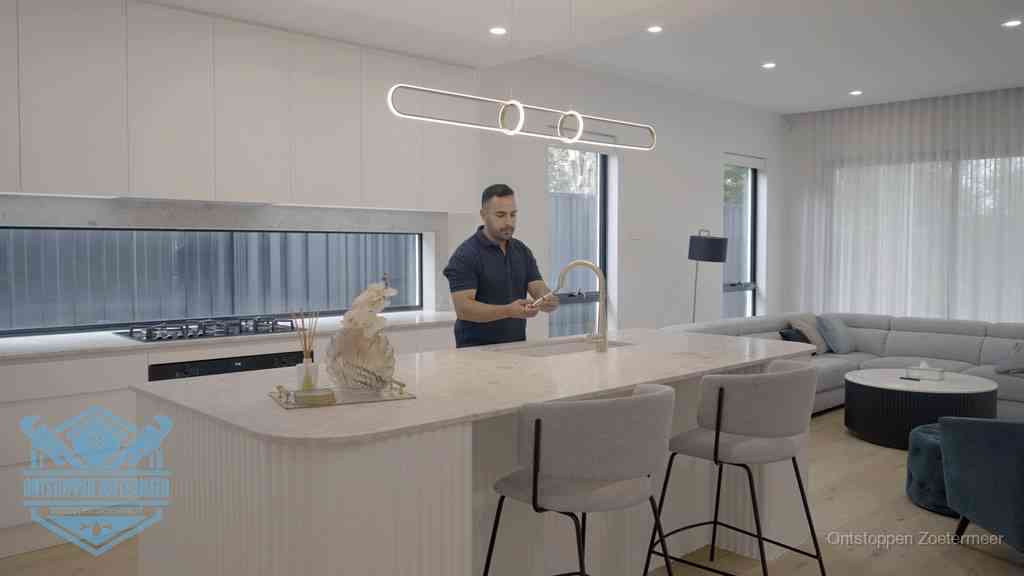 Een bewoner bij de keukenspoelbak die zelf aan de slag gaat met een verstopte gootsteen in Zoetermeer